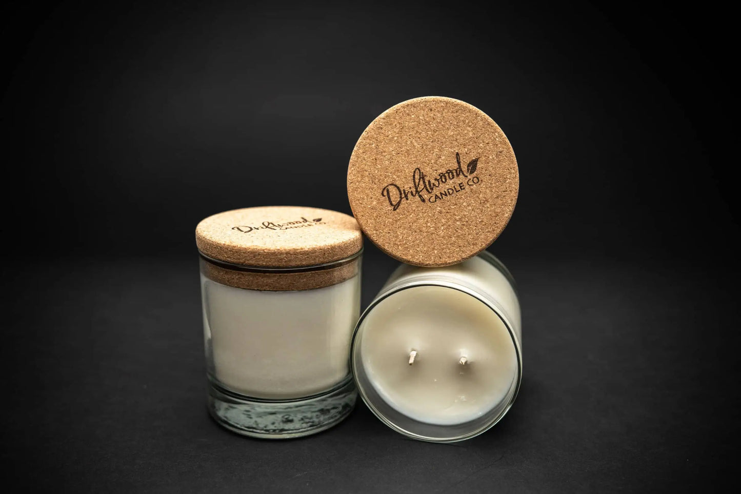 Two scented soy candles on a black background with a cork lid stamped with the Driftwood Candle Co. logo